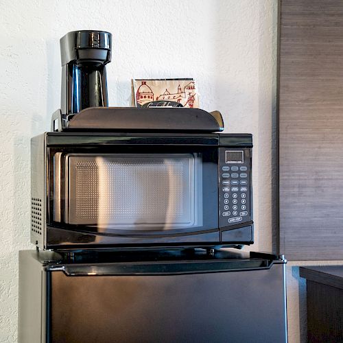 The image shows a compact kitchen setup with a coffee maker on top of a microwave, which is placed on a mini refrigerator.