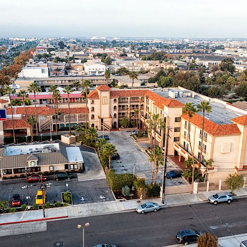 The image shows an aerial view of a cityscape featuring residential buildings, a few businesses, and several cars parked on the street.