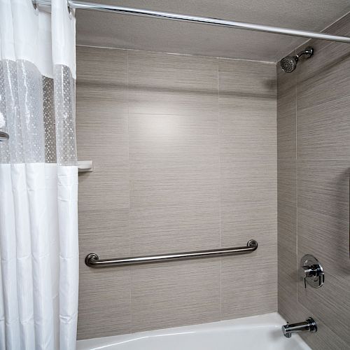 The image shows a bathroom with a shower area that has a white curtain, multiple towel racks, and safety grab bars on the walls.