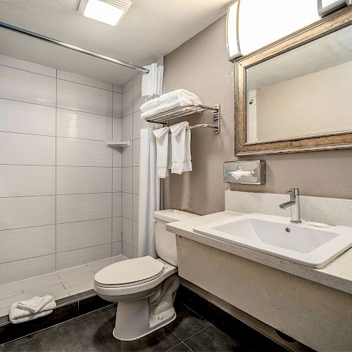 A modern bathroom with a walk-in shower, toilet, sink, large mirror, and towel rack, all in a neutral color scheme, well-lit and clean.