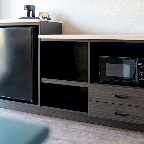 A kitchen counter with a mini-fridge, microwave, coffee maker, and storage drawers against a wall, situated on a hardwood floor.