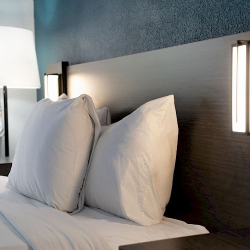 A modern bedroom with a neatly made bed, white pillows, bedside lights, and a floor lamp near a window with patterned curtains.