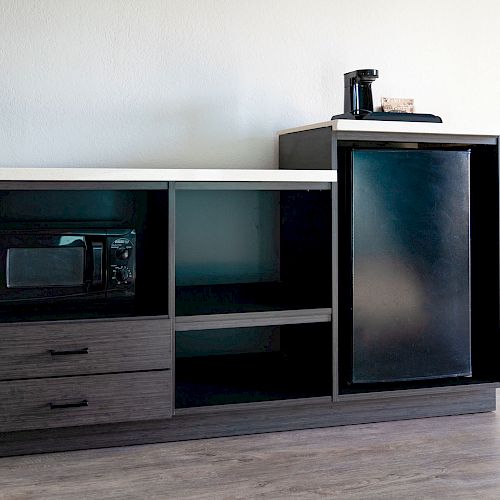 The image shows a black cabinet with a microwave, a mini-fridge, and a coffee maker on top, with drawers and shelves.