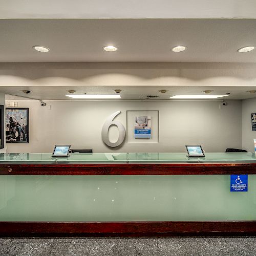 The image shows a motel reception desk with a logo on the wall, brochures, and a sign for accessibility in the foreground.