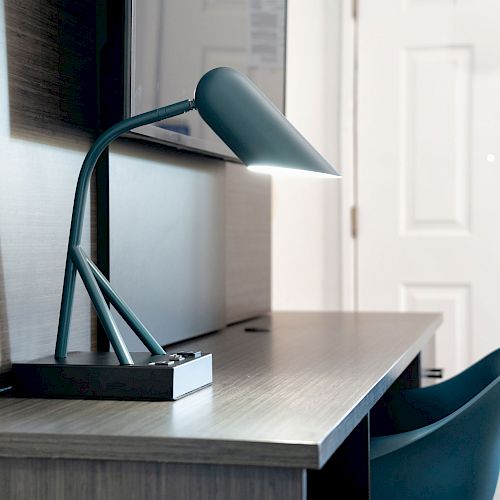 A desk with a modern teal desk lamp, a teal chair, and part of a white door in the background.