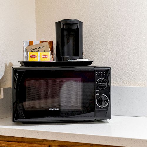 The image shows a countertop with a black microwave oven, a coffee maker, and some tea and coffee products on top of the microwave.